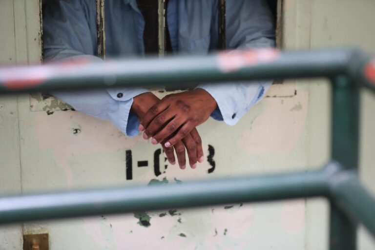 An incarcerated person's arms hang from the window of a jail cell.