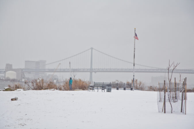 A person takes photos of the Delaware River at Penn Treaty Park in the snow