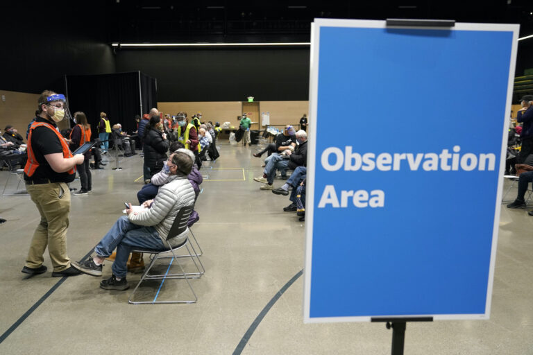 In this  Jan. 24, 2021, file photo, a worker at left checks in with people sitting in an observation area after they were given the first of two doses of the Pfizer vaccine for COVID-19 in Seattle. (AP Photo/Ted S. Warren)