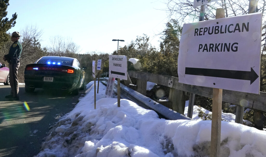 A sign directs Republican and Democrat legislators to their parking areas as a N.H. State Trooper watches the flow of traffic prior to a New Hampshire House of Representatives session held at NH Sportsplex, due to the coronavirus, Wednesday, Feb. 24, 2021, in Bedford, N.H. (AP Photo/Charles Krupa)