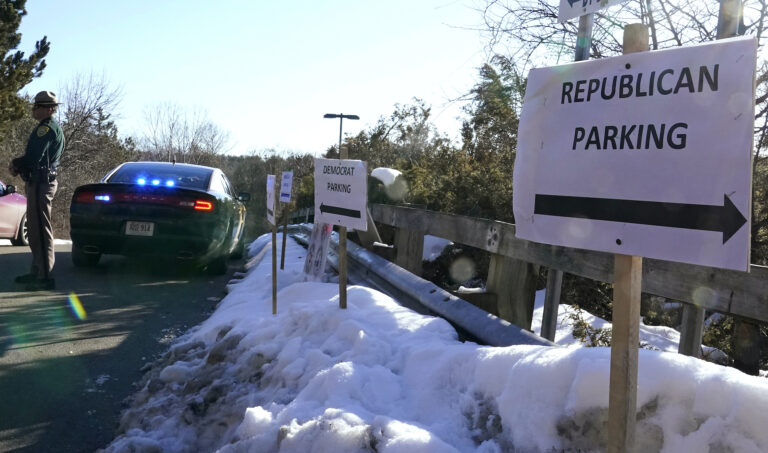 A sign directs Republican and Democrat legislators to their parking areas as a N.H. State Trooper watches the flow of traffic prior to a New Hampshire House of Representatives session held at NH Sportsplex, due to the coronavirus, Wednesday, Feb. 24, 2021, in Bedford, N.H. (AP Photo/Charles Krupa)