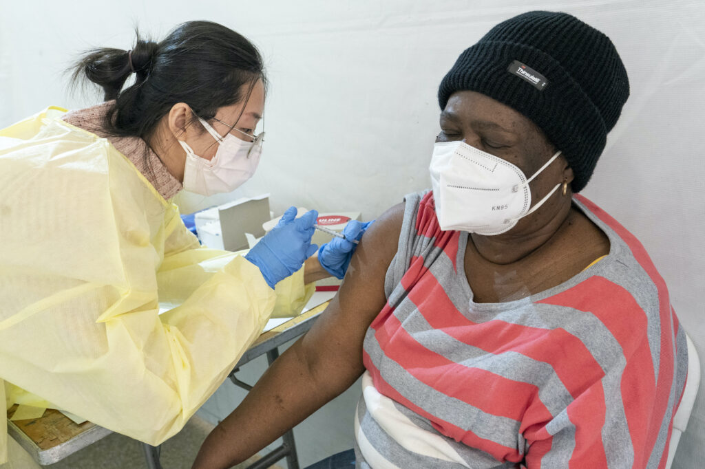 Virus Outbreak US Surge Registered Nurse Shyun Lin, left, gives Alda Maxis, 70, the first dose of the COVID-19 vaccine at a pop-up vaccination site