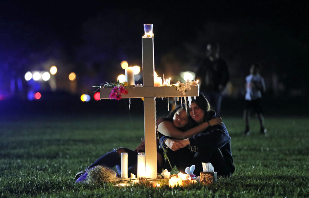 School Shooting Parkland Biden In this Feb. 15, 2018 file photo, people comfort each other as they sit and mourn at one of seventeen crosses, after a candlelight vigil for the victims of the shooting at Marjory Stoneman Douglas High School, in Parkland, Fla. (AP Photo/Gerald Herbert, File)