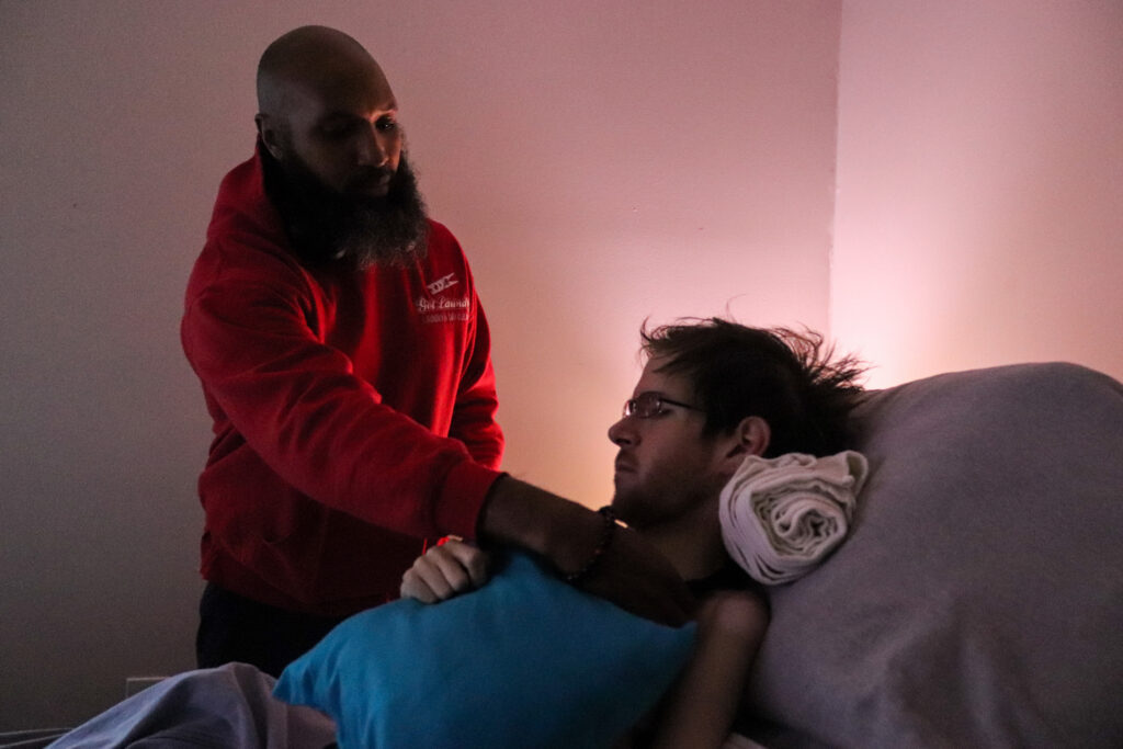 Karas_HomeHealthWHYY-14 Ray Wall, a licensed practical nurse, positions Steven Sebastianelli in his bed. Wall visits Sebastianelli’s apartment every day to assist him in daily living activities. (Madison Karas/WHYY)