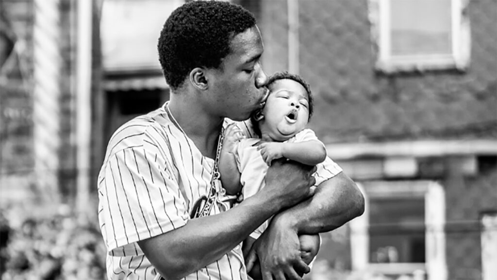 KenMcFarlane A photograph by Ken McFarlane showing a Black father kissing their baby in Movers & Makers: Made with Love