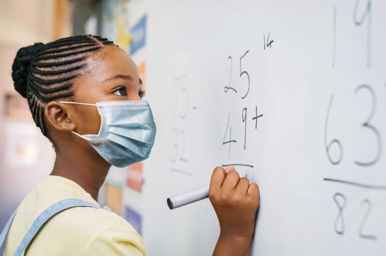 Black schoolgirl solving addition sum on white board during Covid-19 pandemic