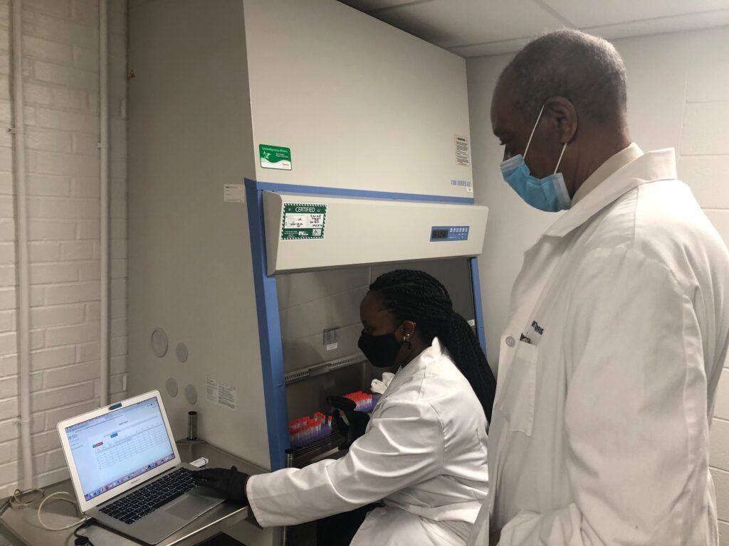 dsu Audrey Janga works with COVID-19 test samples as medical director Dr. Harris Curtis observes. (Cris Barrish/WHYY)