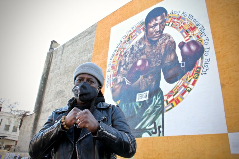 Artist Ernel Martinez in front of a mural of Philadelphia boxer Joe Frazier