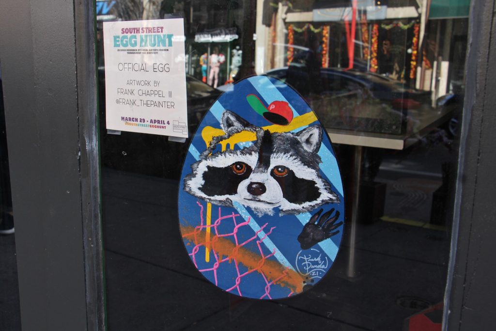 2021 03 30-e lee–philadelphia south street headhouse-easter egg hunt raccoon A decorated Easter Egg hanging in a window on South Street in Philadelphia