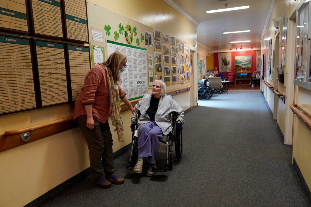 Virus Outbreak Nursing Homes Chaparral House activities director Erika Shaver-Nelson, left, talks with resident Joyce in the hallway at Chaparral House in Berkeley, Calif., Thursday, March 18, 2021. (AP Photo/Jeff Chiu)