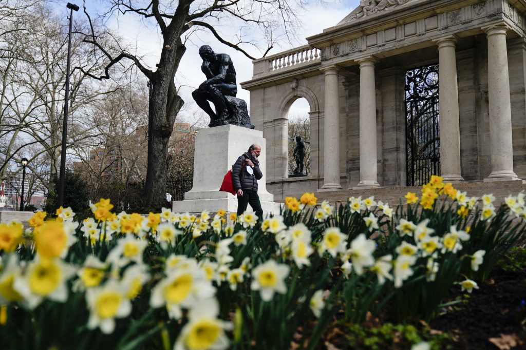 Virus Outbreak Pennsylvania Daily Life A pedestrian holding a face mask walks by daffodils blooming