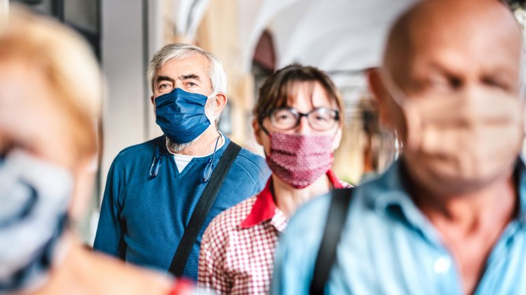Crowd of adult citizens walking on city street wearing face masks