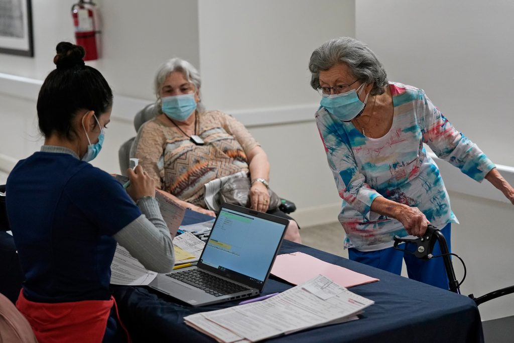 Mitzi Hansrote,Deanna Sutton Mitzi Hansrote, right, 86, and Deanna Sutton, center, 83, check in before receiving the COVID-19 vaccine, Thursday, Jan. 21, 2021, at the Isles of Vero Beach assisted and independent senior living community in Vero Beach, Fla. Government officials placed long-term care residents and staff among their top vaccination priorities after they authorized the emergency use of shots from Pfizer and Moderna in late 2020. (AP Photo/Wilfredo Lee)