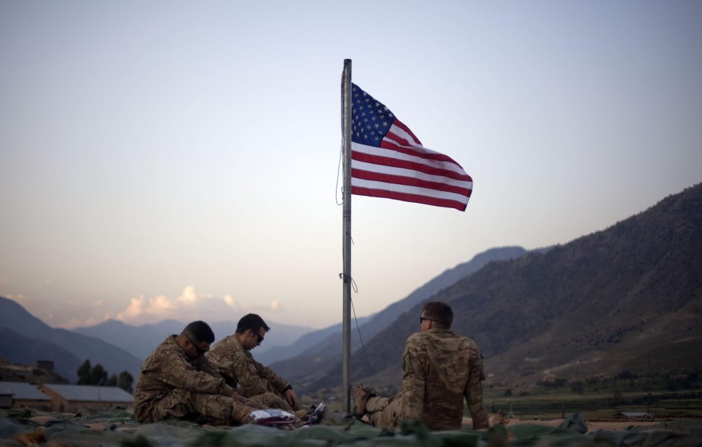 Afghanistan NATO Analysis FILE - In this Sept. 11, 2011 file photo, US soldiers sit beneath an American flag just raised to commemorate the tenth anniversary of the 9/11 attacks at Forward Operating Base Bostick in Kunar province. (AP Photo/David Goldman, File)