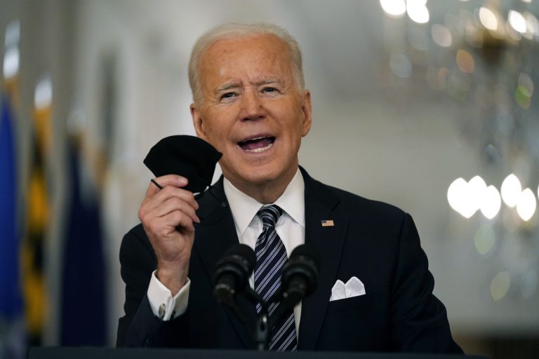 President Joe Biden holds a mask in his hand as he speaks from a podium