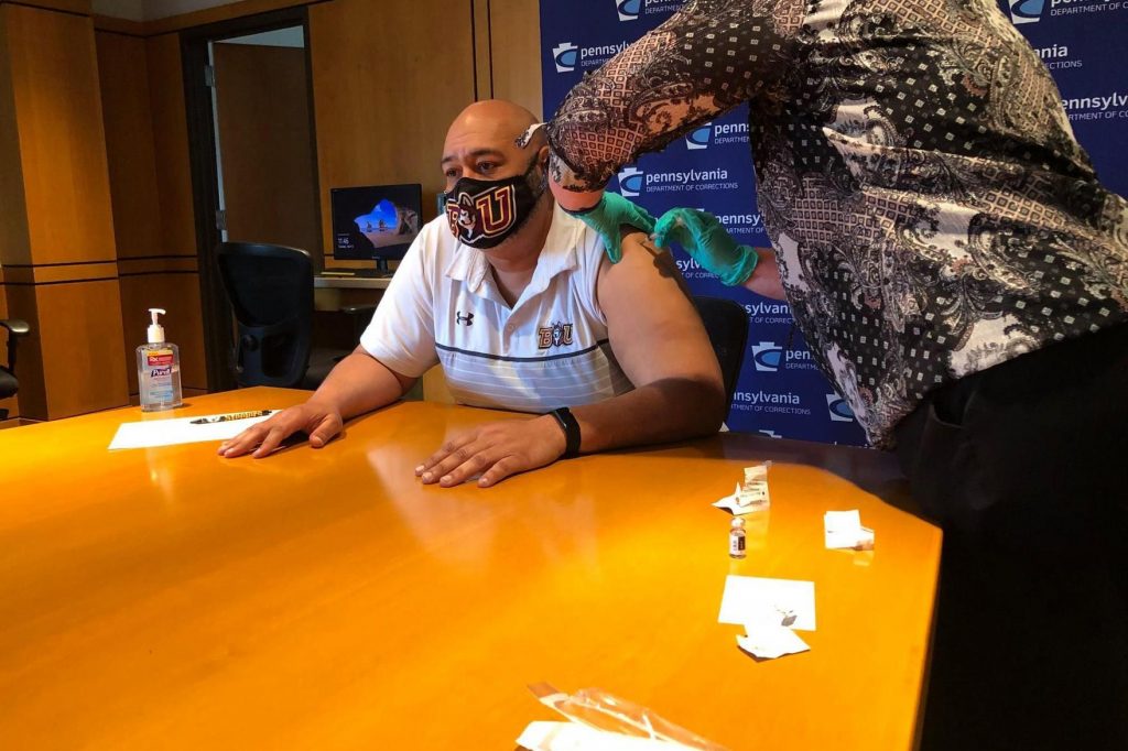 A person receives the COVID-19 vaccine while sitting at a large table