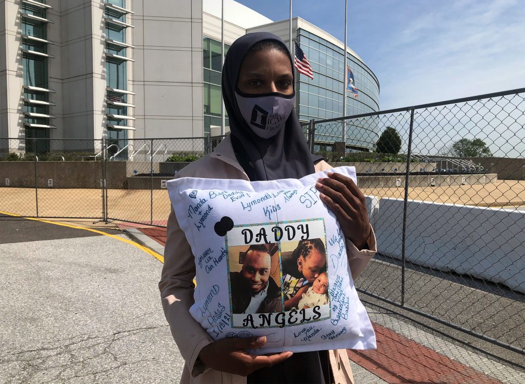 amanda-in-front-of-station Amanda Spence holds a pillow with photos of her slain husband Lymond Moses and their two children in front of New Castle County police headquarters. (Cris Barrish/WHYY)