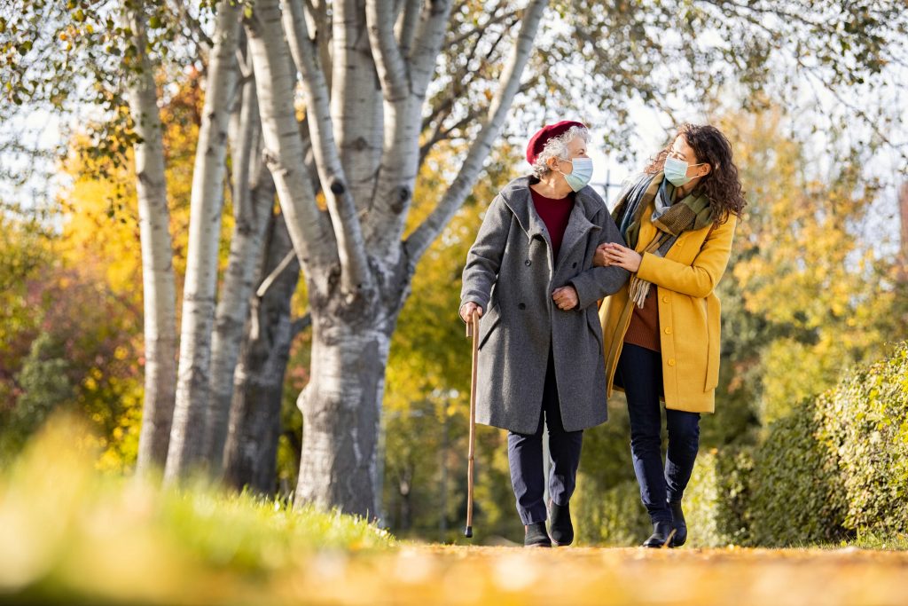 Granddaughter walking with senior woman in park wearing face mas Granddaughter walking with senior woman in park wearing face mask for safety against covid-19