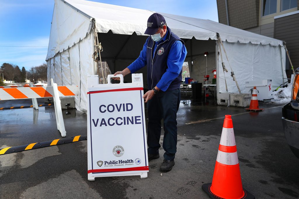 Nearly a third of adults in the U.S. have gotten at least one shot of the COVID-19 vaccine so far, but researchers warn that vaccine refusal may keep the country from reaching herd immunity. A health worker stands next to a COVID-19 vaccine sign