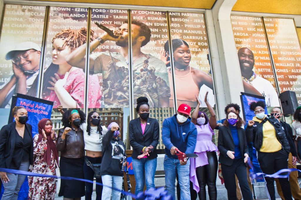 2021-05-11-k-paynter-crown-mural,-russell-craig Mural artist Russell Craig cuts the ribbon on the West side of Philadelphia’s Municipal Services Building at the dedication of the Crown mural on May 11, 2021. (Kimberly Paynter/WHYY)