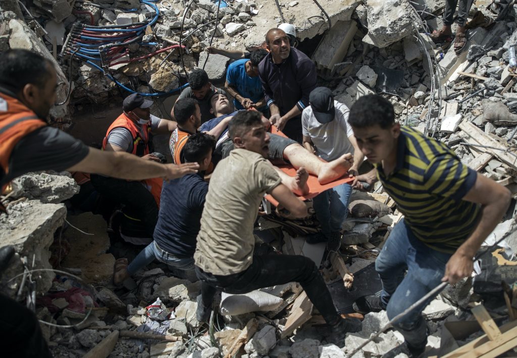 Palestinian rescuers carry a survivor man from under the rubble of a destroyed residential building following Israeli airstrikes
