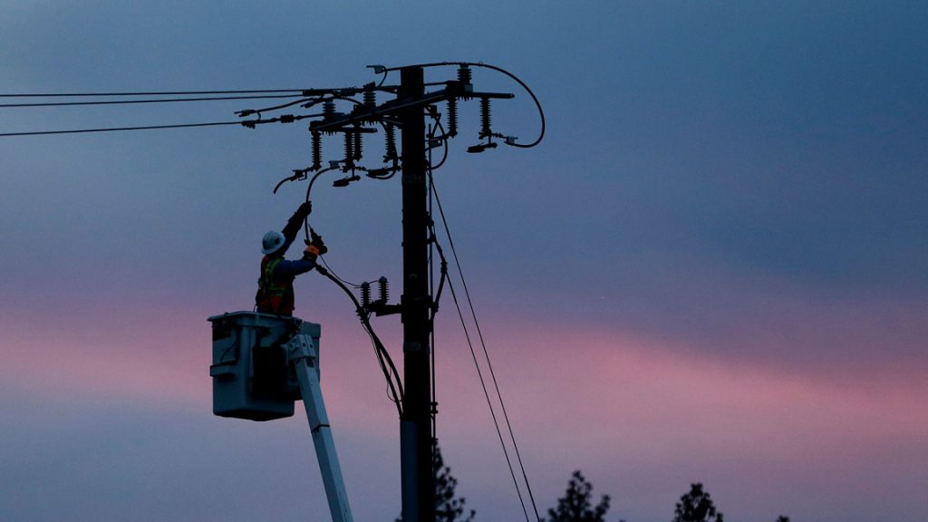 AP_utility-worker-power-line-electric-energy-electricity A utility crew member works the lines against a cotton candy sky