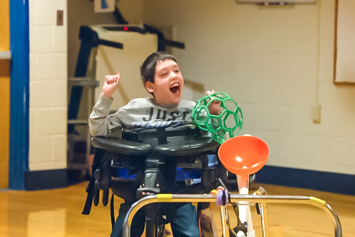 A young boy in a wheelchair having fun in gym class
