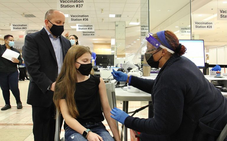 Jenna Baron, 12, of Voorhees, N.J., gets her first Pfizer COVID-19 shot from registered nurse Samantha Hickson at the Burlington County mega site in Moorestown. She is accompanied by her father, Robert Baron, a Vice President of operations for Virtua Medical Group. (Emma Lee/WHYY)