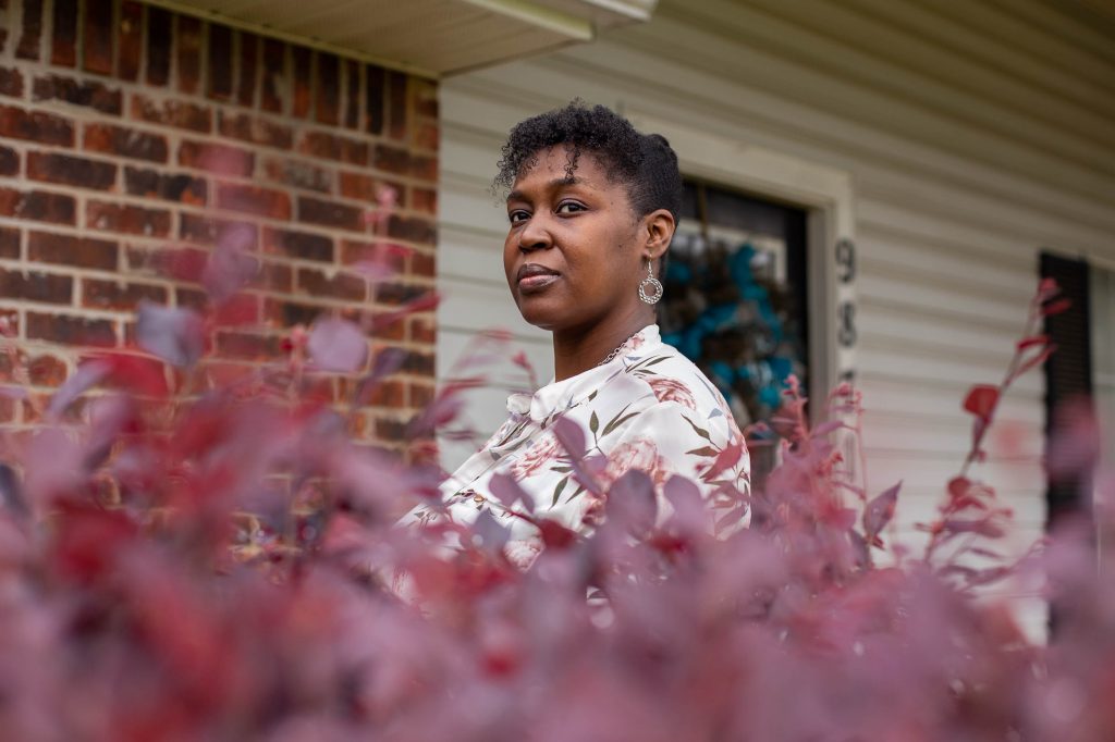 Tia Cunningham stands in front of her home in Byram, Miss., on Wednesday. She’s a past recipient of a guaranteed income pilot project in Jackson, and it helped her save up for a down payment. Tia Cunningham stands in front of home, with plant leaves in the foreground