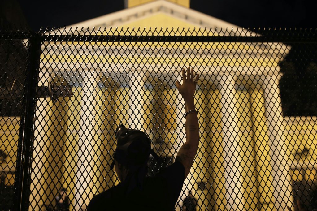 A protester calls out to police standing guard behind security fencing