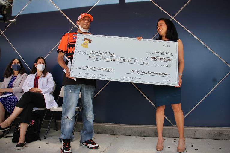 Vaccine sweepstakes winner Daniel Silva and Dr. Angela Duckworth hold a giant check during a press event at Maria de los Santos Health Center. (Emma Lee/WHYY)