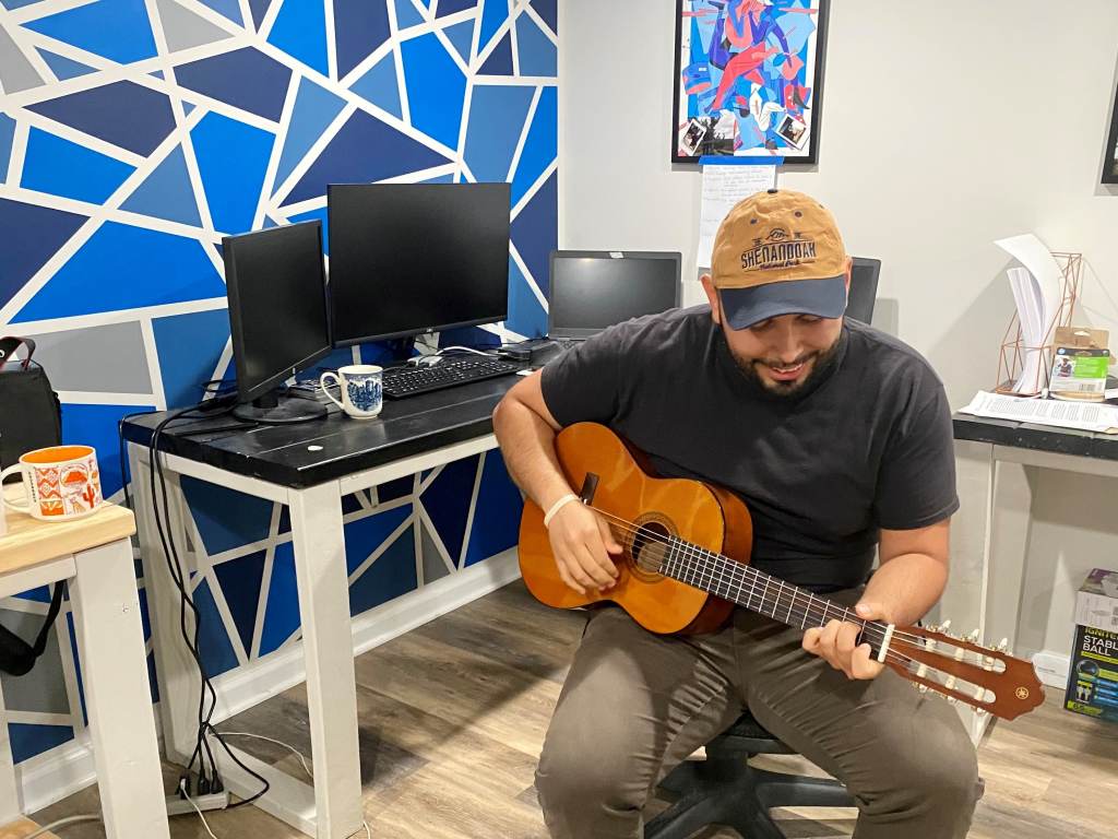 Jonathan plays the guitar while sitting at a computer desk