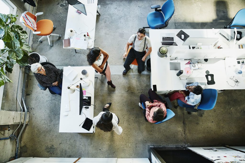 As companies welcome back their employees, many people will have to think about what to wear to work for the first time in over a year. Overhead view of design team having project meeting in office