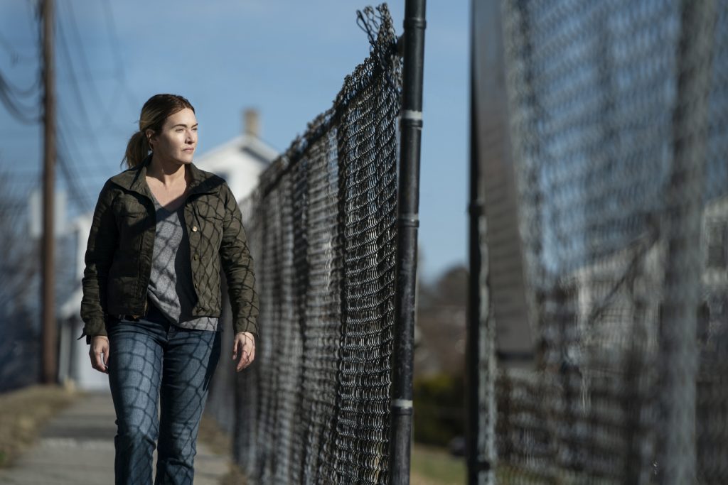 Kate Winslet, portraying her character Mare, walks along a fence