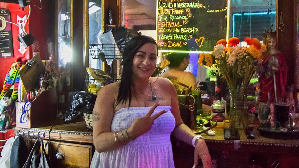 Sheila throws up a peace sign while tending bar