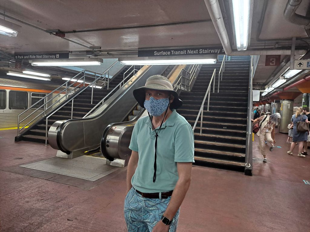 Collin Sundt wears a face mask while standing at the bottom of an escalator