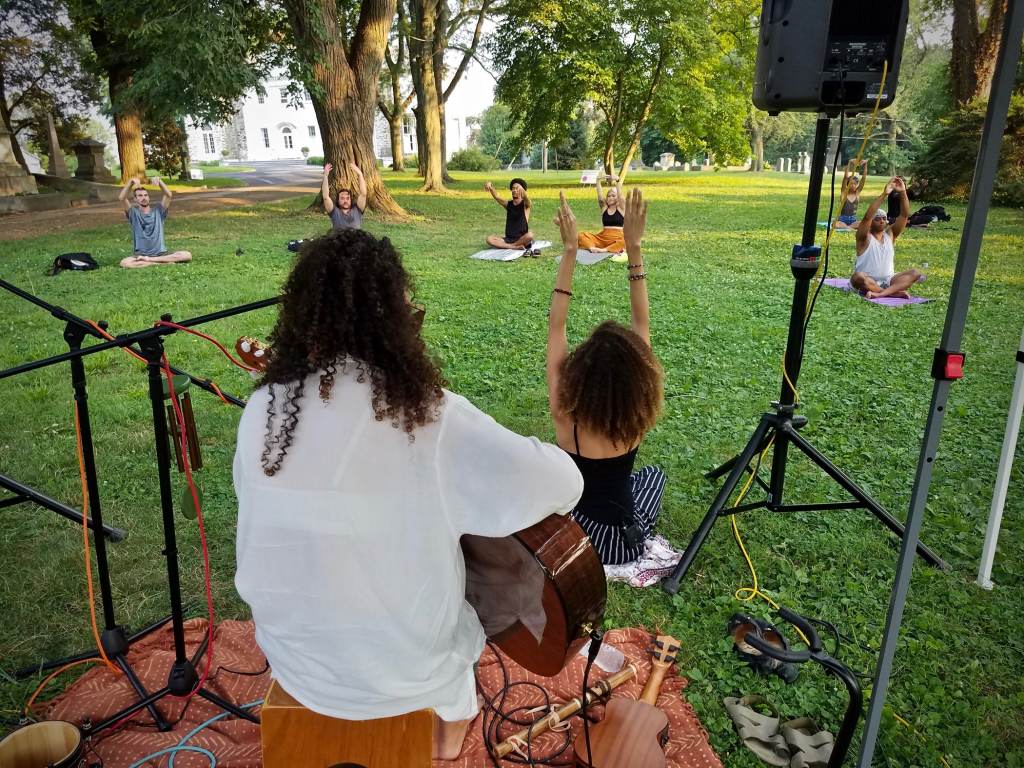 2021 07 07-p crimmins-alexia oliveira aubrey howard-philadelphia woodlands cemetery-yoga and jazz Aubrey Howard (in black tank) leads a session of intentional breathing meditation, accompanied by musician Alexia Oliveira, during a yoga session at the Woodlands cemetery. (Peter Crimmins/WHYY)