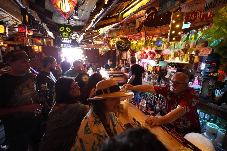 FILE - In this Wednesday, July 7, 2021, file photo, patrons enjoy cold tropical cocktails in the tiny interior of the Tiki-Ti bar as it reopens on Sunset Boulevard in Los Angeles. COVID-19 cases have doubled over the past three weeks, driven by the fast-spreading delta variant, lagging vaccination rates in some states and Fourth of July gatherings.  Los Angeles County public health officials have urged people to resume wearing masks indoors regardless of their vaccination status. (AP Photo/Damian Dovarganes, File)