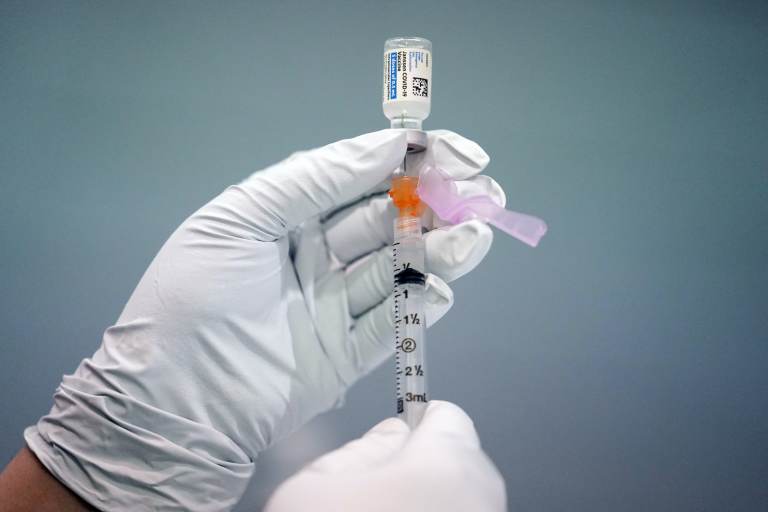 A gloved hand holds up a syringe of the COVID-19 vaccine