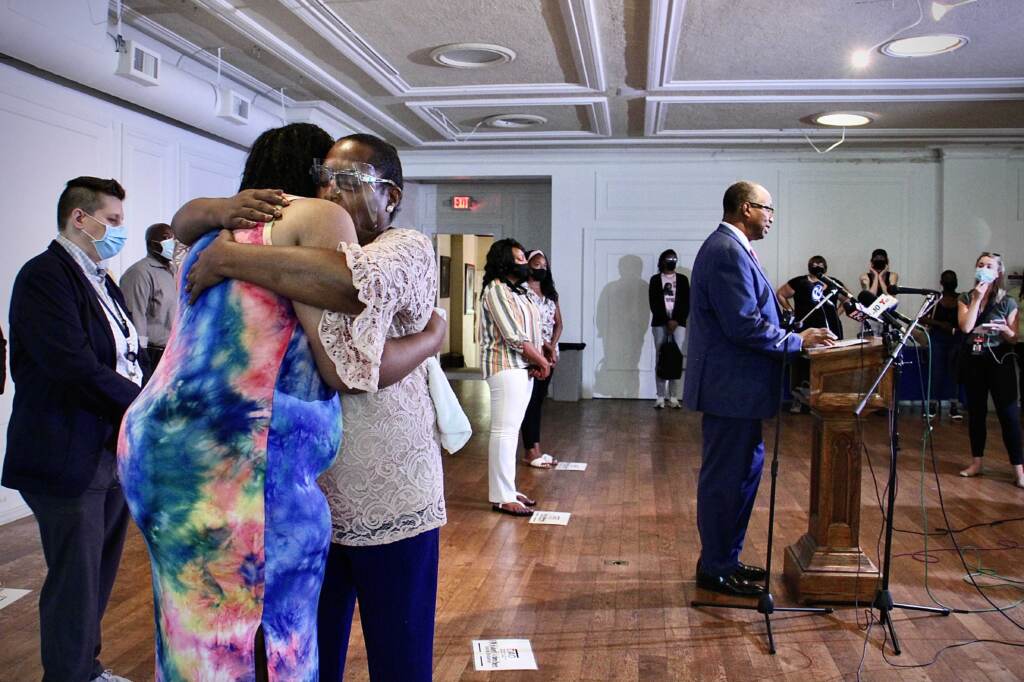 DAO_homicides_presser_EL_072621_01 Rev. Andrea Harrington comforts Crystal Davis, with a speaker standing at a podium in the background