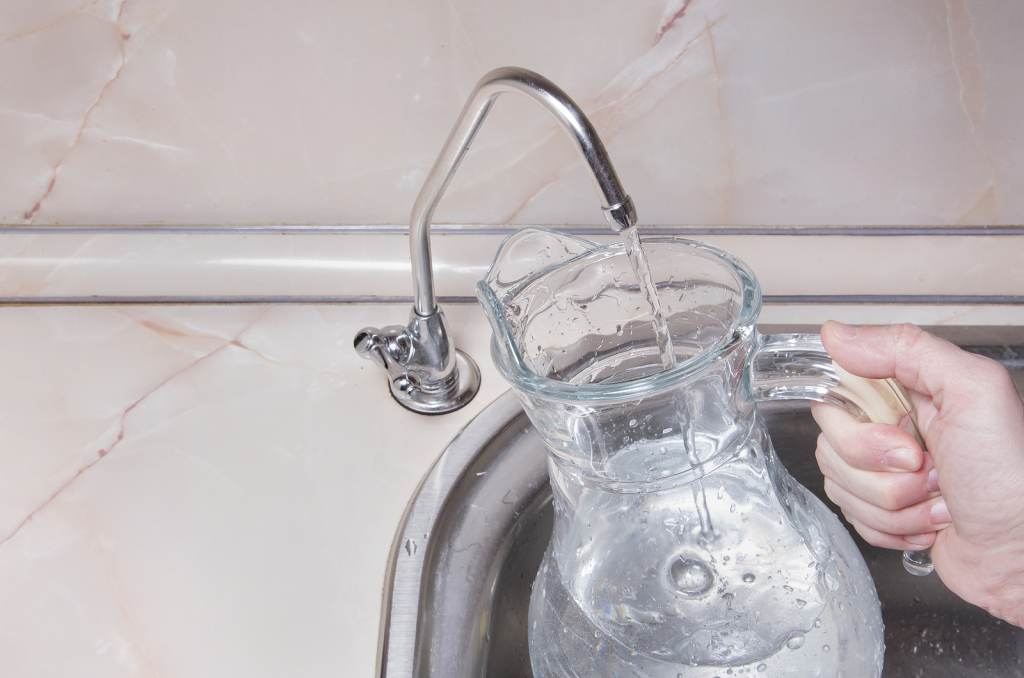 Pouring Drinkable Water Into Glass Jug From Water Filter. Closeu A person fills up a jug of water from a faucet.