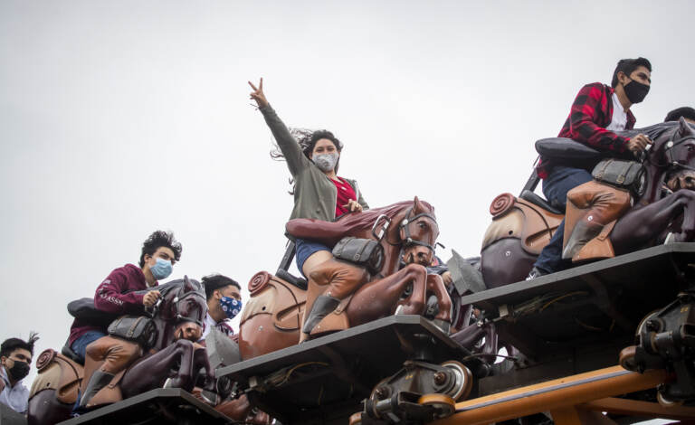 Park patrons ride the Pony Express roller coaster ride, one pictured in center wearing a mask and throwing up a peace sign