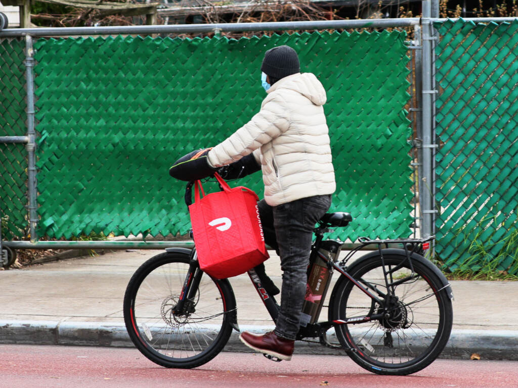 A DoorDash delivery person rides their bike in New York City. Workers across the country went on strike on July 31 to demand higher pay and tip transparency. A DoorDash delivery person rides their bike