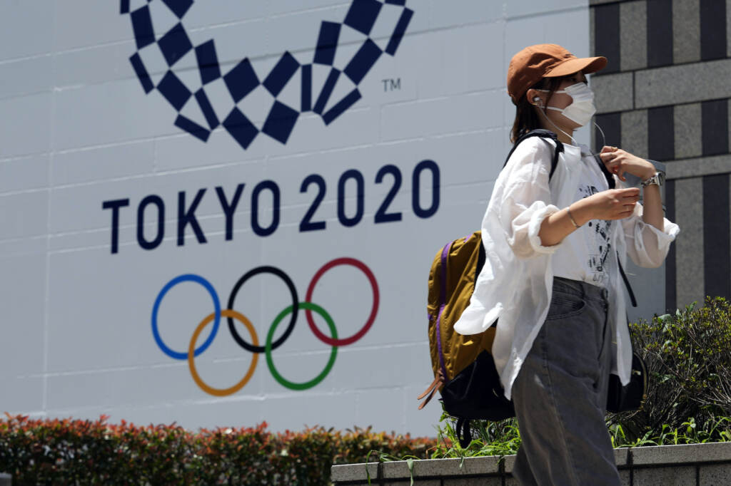 Unusual Olympics A woman wearing a protective mask walks with a baseball cap to shield from the sun walks in front of a Tokyo 2020 display