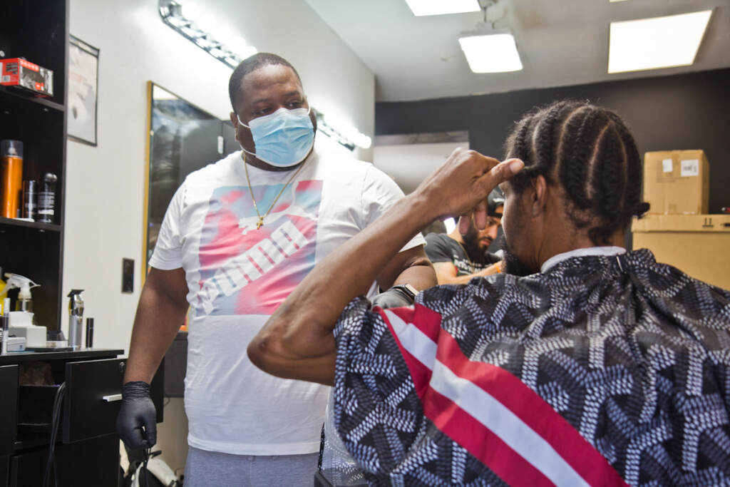 Javan Rankines gives someone a haircut while wearing a face mask