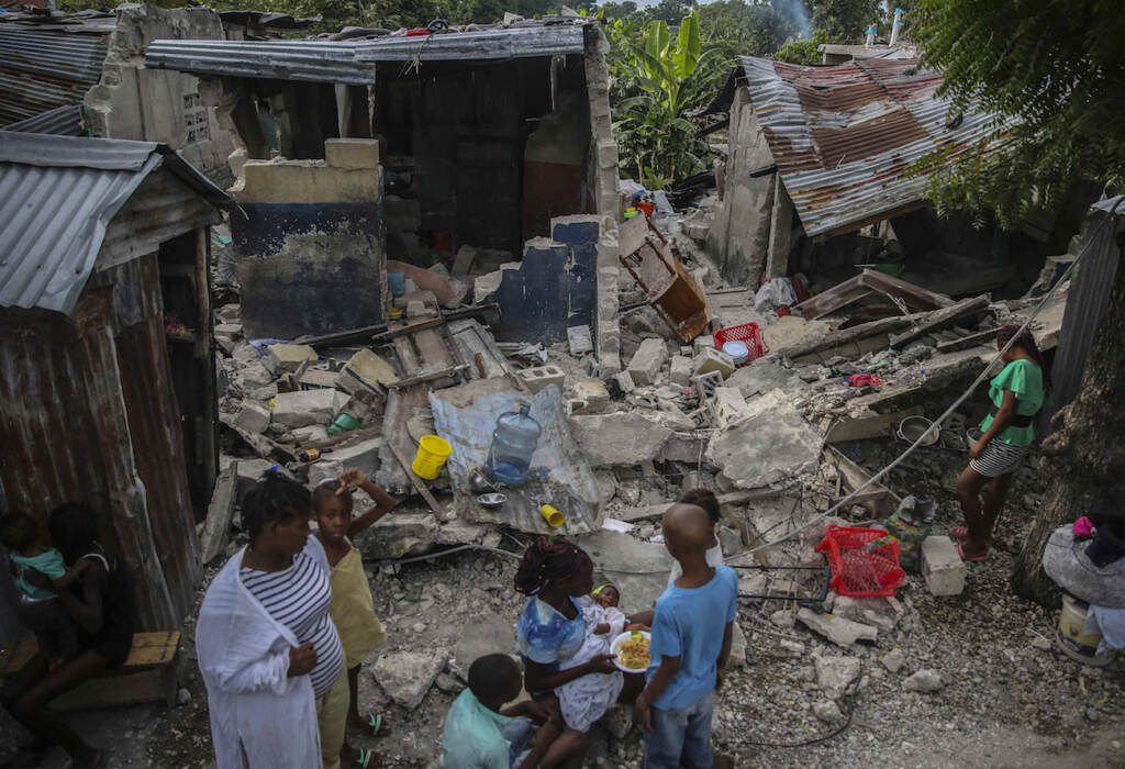 APTOPIX Haiti Earthquake A family eats breakfast in front of homes destroyed by a 7.2 magnitude earthquake in Les Cayes, Haiti, Sunday, Aug. 15, 2021. (AP Photo/Joseph Odelyn)