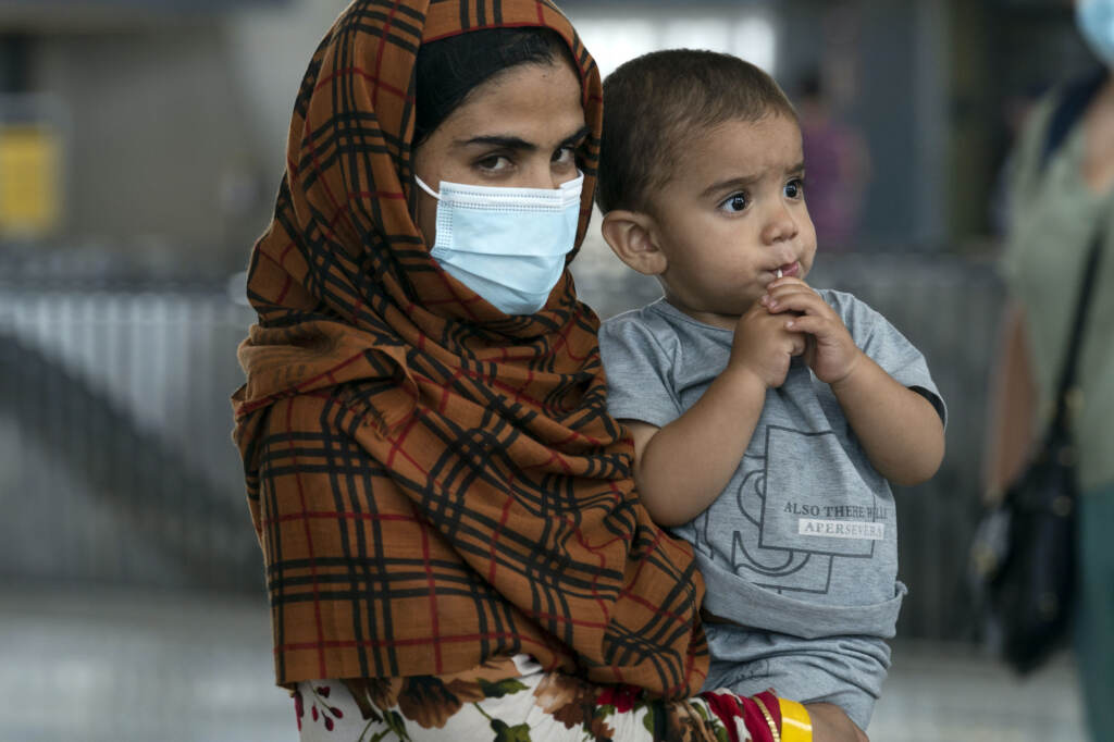 An Afghan woman wearing a face mask holds a child