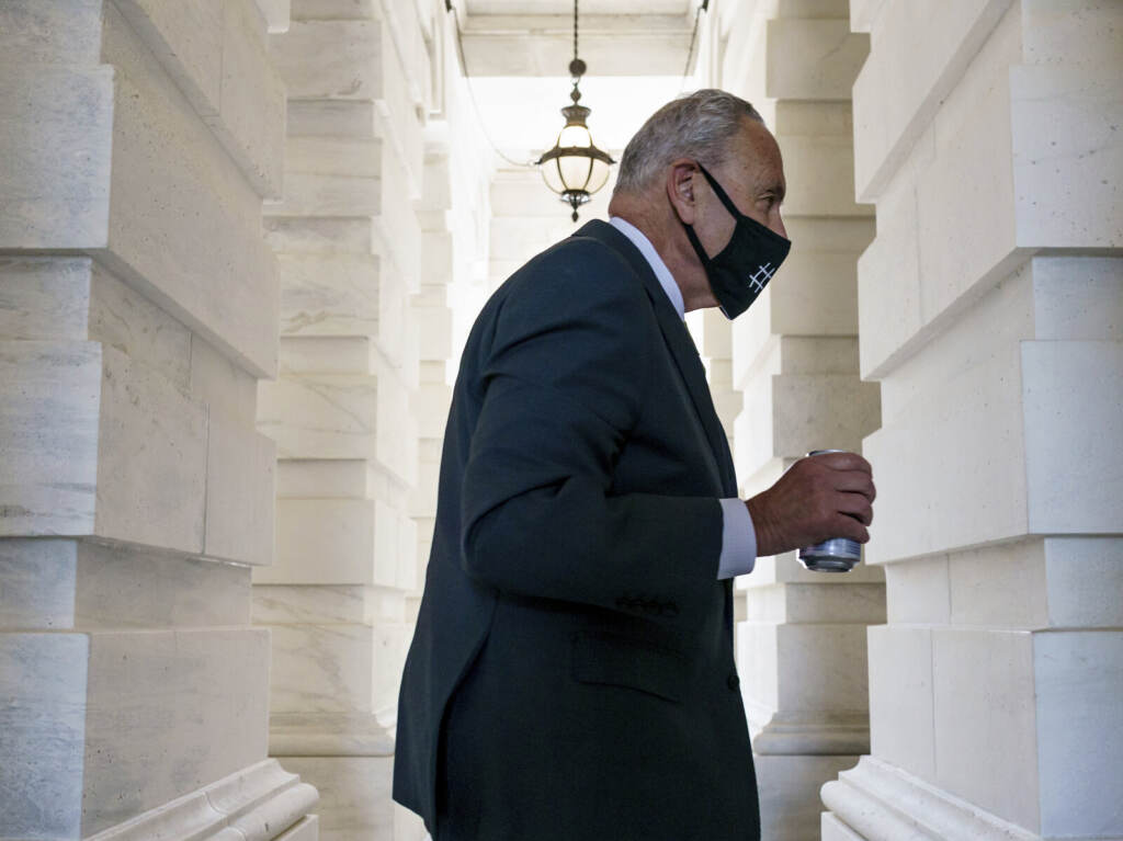 Chuck Schumer Chuck Schumer walks while carrying a beverage and wearing a mask