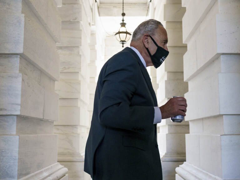 Chuck Schumer walks while carrying a beverage and wearing a mask