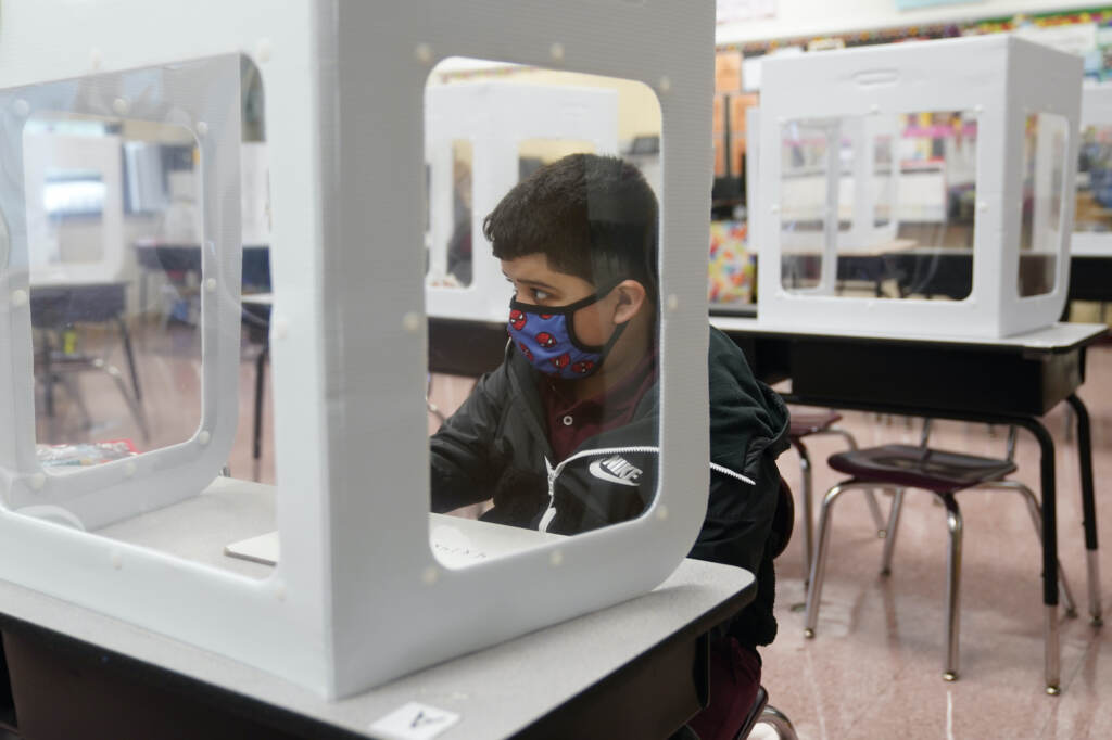 Virus Outbreak New Jersey Julian Aldridge wears a face mask while sitting at a desk behind a see-through partition